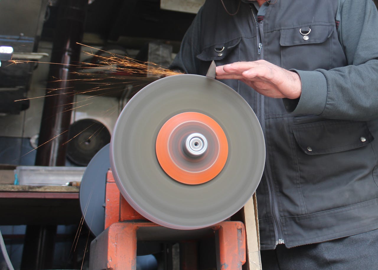 Services-02 A close-up of a man working with a grinding machine in a workshop, sparks flying.