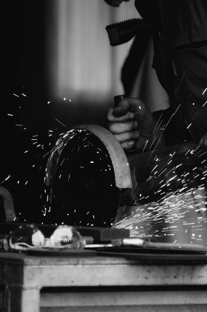 Black and white photograph of a craftsman creating sparks while cutting metal in a workshop.