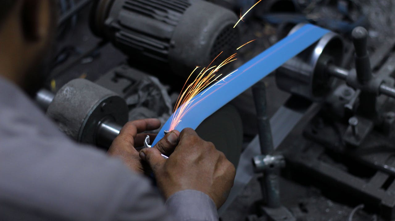 Services-03 Close-up of hands grinding metal with sparks in an industrial workshop.