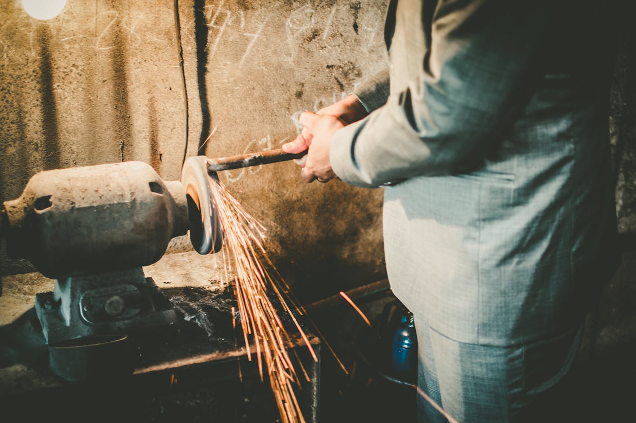 Services-01 Close-up of a man in a suit using a grinder in an industrial setting with sparks flying.